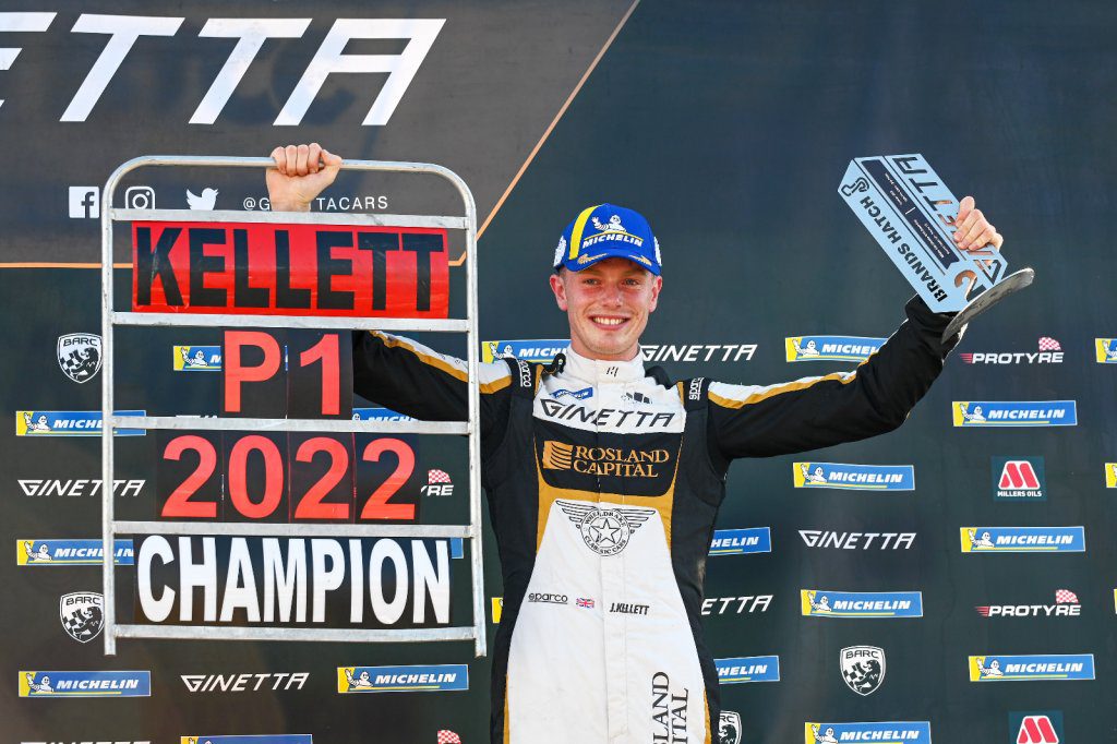 James Kellett on a racing podium holding up his trophy and champion announcement