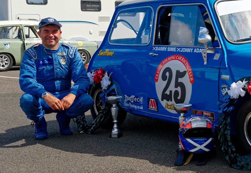Barry Sime, wearing his blue race suit, crouched next to his blue mini.