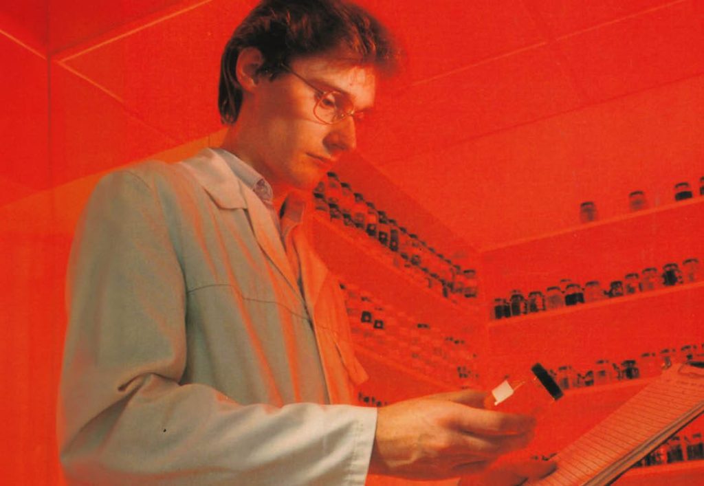 Red photo of Peter as the laboratory technician looking at a small container and a clipboard